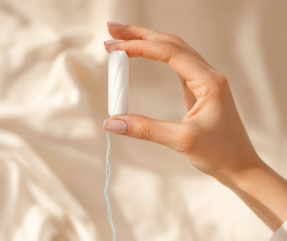 Ruka drží bavlněný tampon nad krémovým lněným prostěradlem